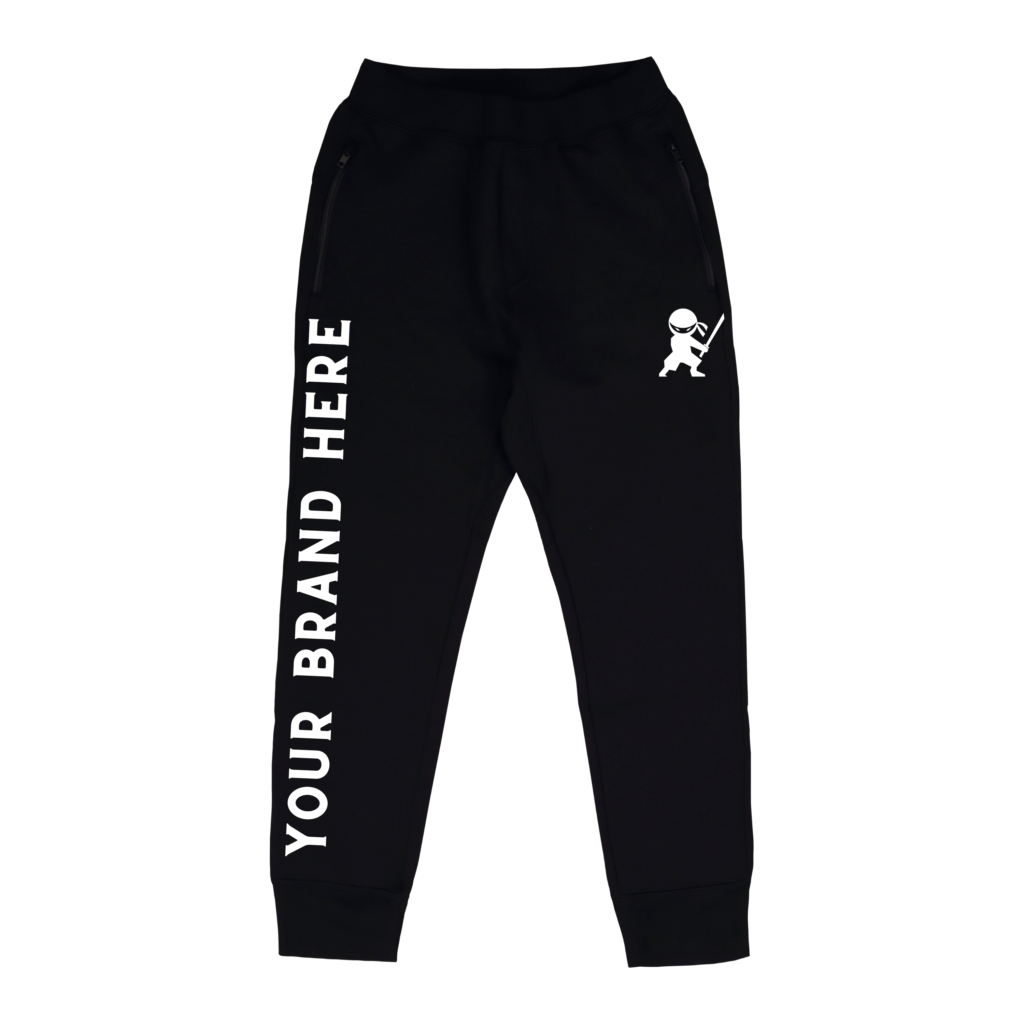 A pair of black sweatpants with a ninja design underneath the left pocket. There is text on the right leg that reads "Your Brand Name Here".