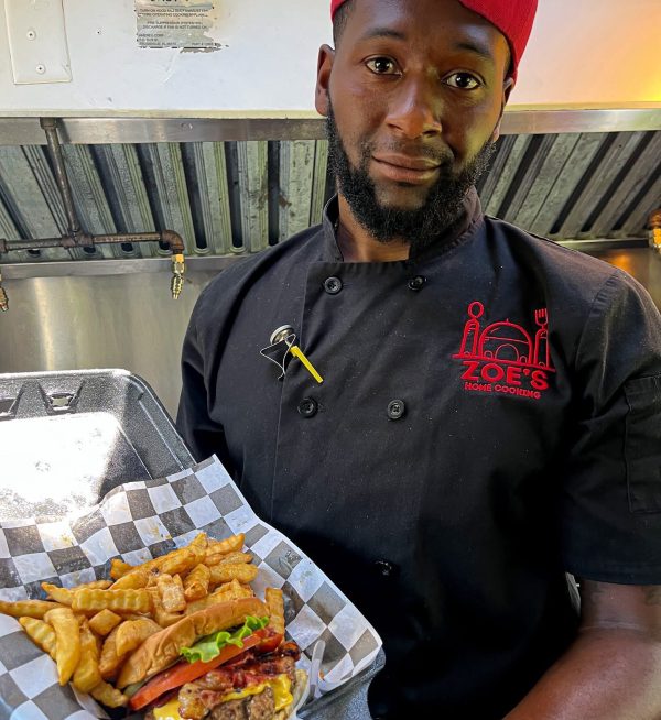 Restaurant owner wearing a custom embroidered chef coat produced by Put It On A Shirt, etc. while serving food in a commercial kitchen.